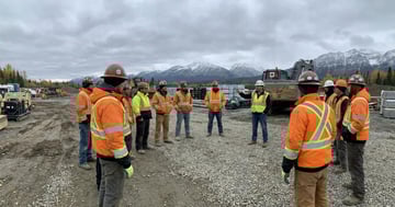 Canadian construction workers in hi-vis winter jackets gathered for a morning safety briefing with Rocky Mountains in the background
