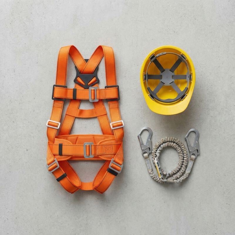 Flat-lay photo of fall arrest equipment including a full-body harness, hard hat, and shock-absorbing lanyard laid out on a surface