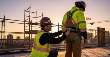 Safety trainer adjusting a fall protection harness on a construction worker on a rooftop construction site in Canada