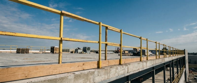 Wide shot of temporary guardrail edge protection installed along the perimeter of a commercial building rooftop under construction
