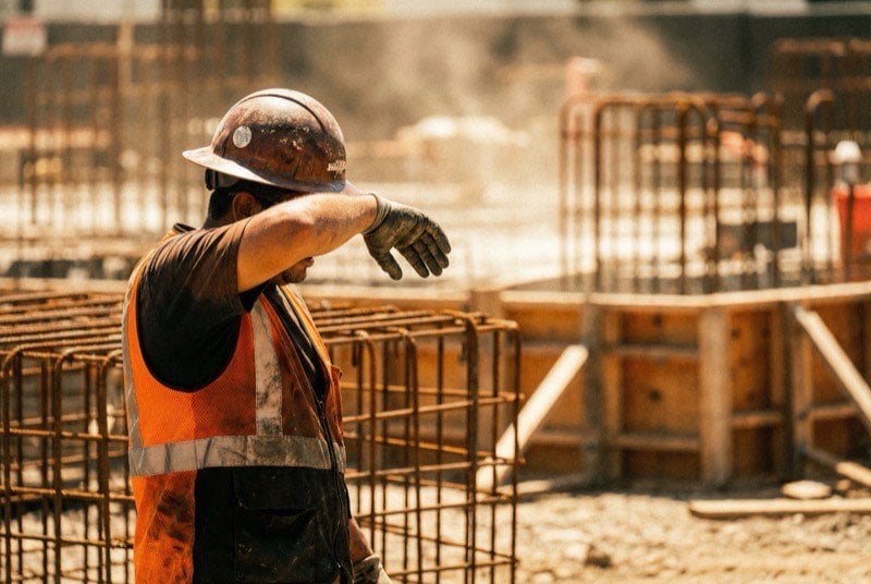 Construction worker wiping sweat from forehead in harsh midday sun on a concrete formwork job site